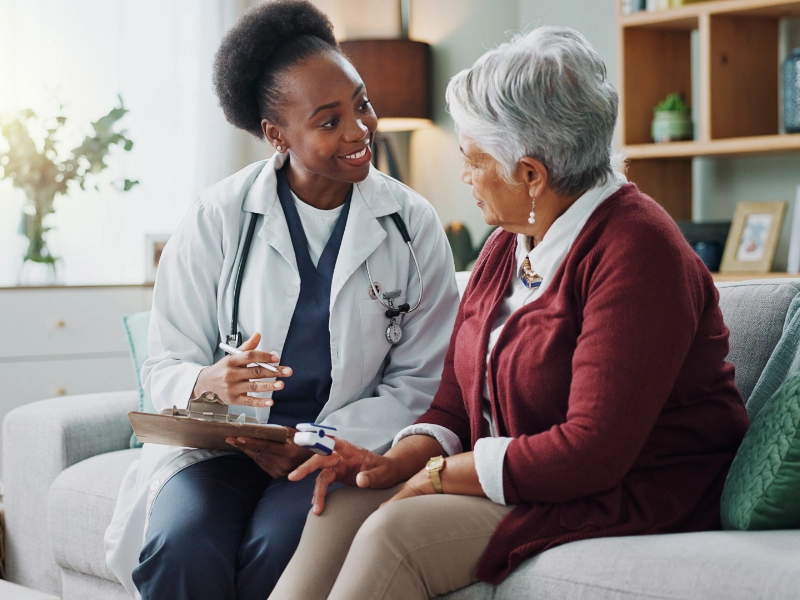 A nurse talking to a woman on her couch.